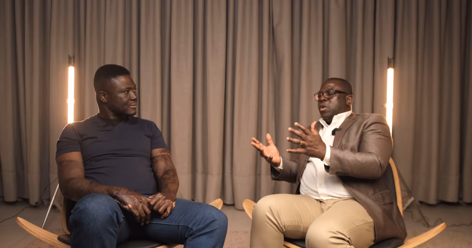 Pierre is seated with Naa Oyoo Kortey of Channel1 in a studio set having a conversation, with a large screen showing a smiling man in the background.