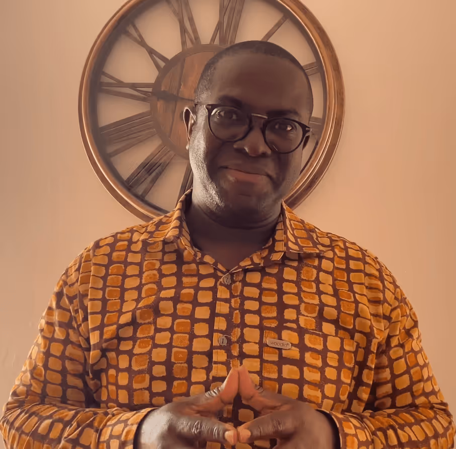 Dr Yaw Perbi is standing in front of a wall clock with Roman numerals endorsing Pierre's book