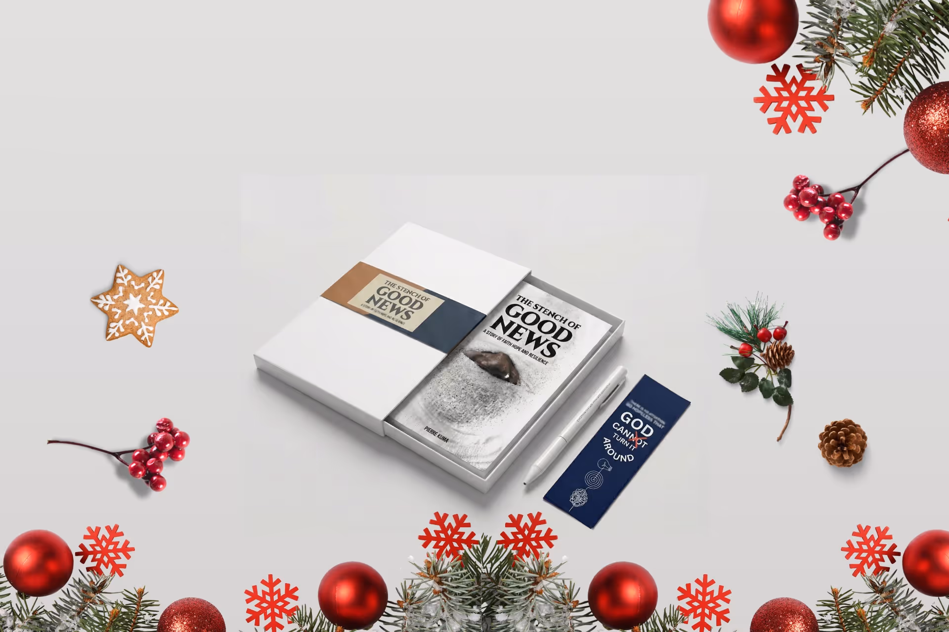 Holiday-themed gift set with a book titled 'The Stench of Good News', a white pen, and a navy bookmark, surrounded by festive decorations including red ornaments, pinecones, berries, and snowflakes.